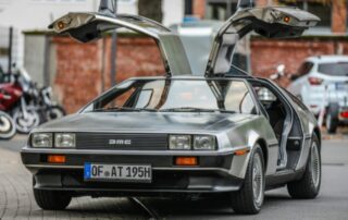 DeLorean DMC-12 grigia con le porte ad ali di gabbiano aperte, parcheggiata in strada