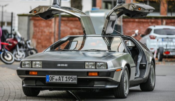 DeLorean DMC-12 grigia con le porte ad ali di gabbiano aperte, parcheggiata in strada