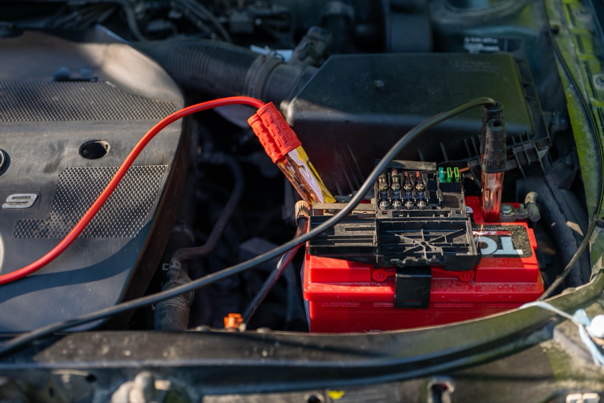 Pinze di un caricabatterie collegate ai morsetti della batteria di un'auto a cofano aperto